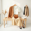 Neatly styled womens outfits with blazer, midi skirt, crossbody bag, and neutral accessories on a bench