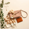 A coordinated set of jewelry, a silk scarf, and a mini bag with a ribbon on a neutral background