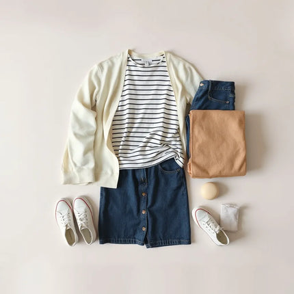 Woman’s everyday outfits arranged neatly with denim, a cardigan, and sneakers on a neutral backdrop