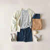 Woman’s everyday outfits arranged neatly with denim, a cardigan, and sneakers on a neutral backdrop