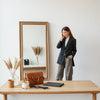 Woman in a tailored blazer and refined outfit with a small bag and delicate jewelry near a mirror