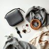 Minimal everyday accessories laid out on a neutral tabletop: bag, watch, jewelry, and a scarf