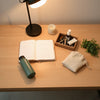 Minimal morning tabletop with a planner, water bottle, keys tray, grooming items, and warm lamp light
