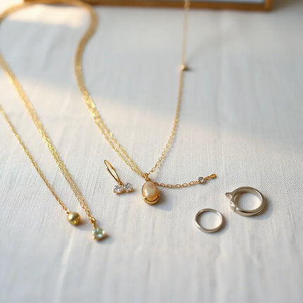 Layered gold and silver necklaces with classic earrings and bracelet on a neutral linen surface