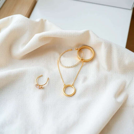 Gold necklace, small earrings, and a slim bracelet arranged on light linen in soft natural light.
