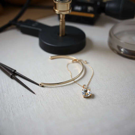 Delicate gold bracelet and pendant on linen beside jeweler tools under soft studio lighting