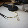Delicate gold bracelet and pendant on linen beside jeweler tools under soft studio lighting