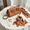 Layered jewelry, a leather handbag, a belt, earrings, and a silk scarf styled on neutral fabric