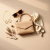 Gold jewelry, a silk scarf, and a mini handbag styled together on a neutral background