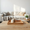 Cozy living room with neutral sofa, styled décor, scented candle, and warm natural light