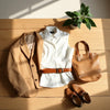 Curated neutral outfit essentials including blazer, shirt, tote, belt, watch, and sleek shoes on a wooden table