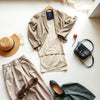 Neutrals wardrobe essentials laid out neatly: blazer, knit top, midi skirt, shoes, and crossbody bag.